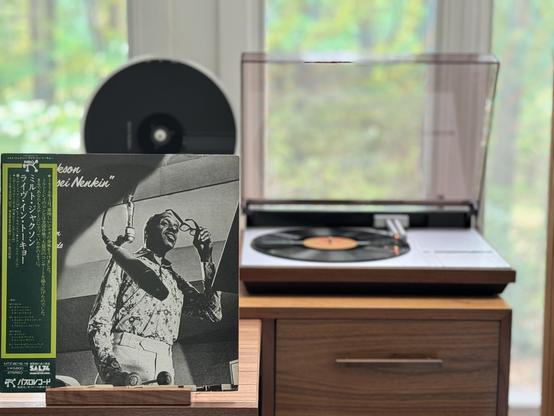 Milt Jackson - At the Kosei Nenkin LP cover.

Bags, removing his glasses, mallets in his right hand, mic in front of him, pointed at his vibes. An OBI strip runs down the left, covering most of the title.

The black LP plays on a vintage Bang & Olufsen Beogram 4000 linear-tracking turntable to the right.