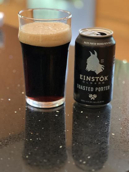 A pint glass of beer with a black can to the right. The can has silver lettering and a bold Viking horned helmet in silhouette
