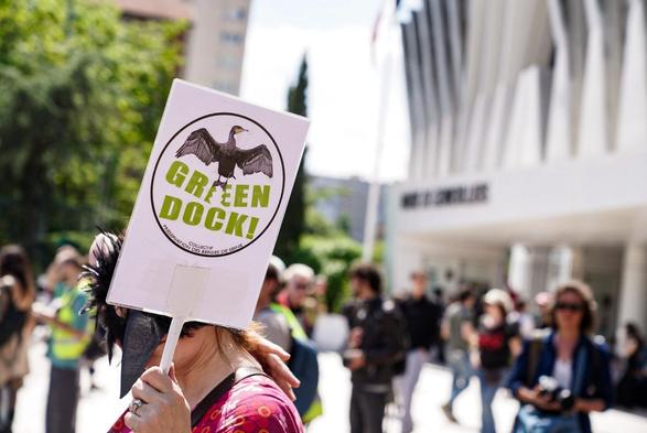 Une manifestante portant une pancarte Gree Dock, illustrée d’une silhouette d’oiseau
