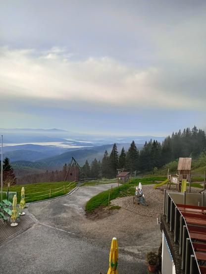Morning view from the mountain too and the valley below that has large misty places. The foreground is lush green while colors fade more to blue the further into the background you look.