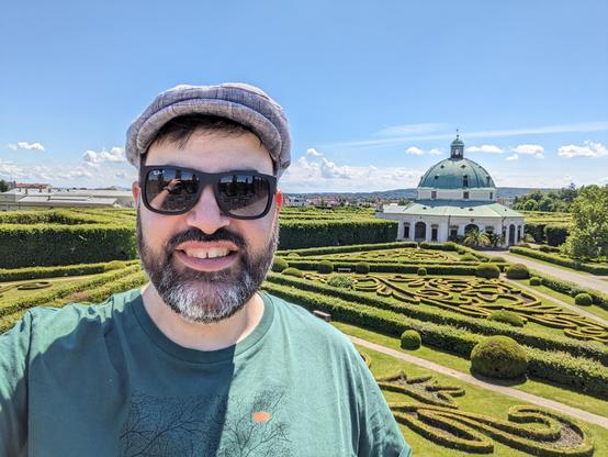 Keywan Selfie erhöht von der Galerie auf den Blumengarten, Hecken in geometrischen Formen und verschiedenen Mustern, Pavillon in der Mitte.