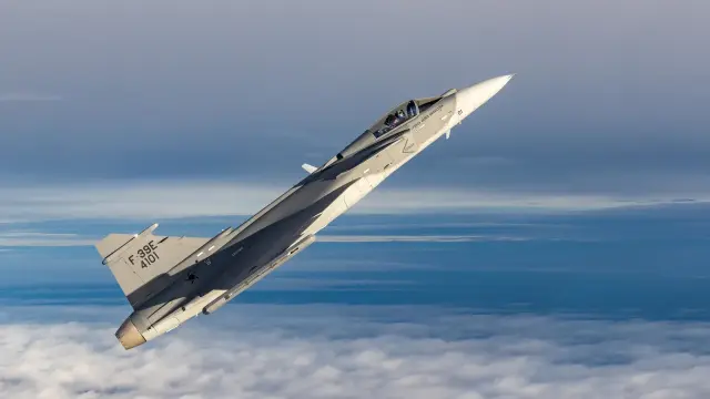 A Brazilian Saab JAS 39 Gripen E doing a sharp vertical climb over a sea of clouds.