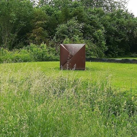 Kunstwerk auf einer grünen Wiese mit Bäumen im Hintergrund.