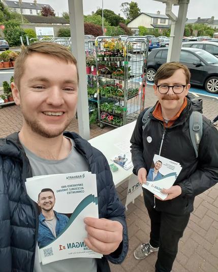 A selfie of Killian and Eoghan with the table with leaflets behind them.
