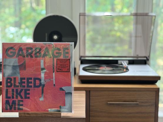 Garbage - Bleed Like Me LP cover.

Bold, san-serif band name and title. A blocky red  tape covers a black and while photo of something…it’s mostly tape, with some staples.

The black LP plays on a vintage Bang & Olufsen Beogram 4000 linear-tracking turntable to the right.