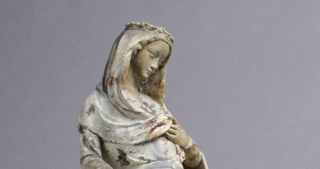 This is a detailed image of an early 14th century French sculpture of the Virgin Mary at the moment of the Annunciation. It is delicately carved limestone with traces of paint. It was made in Paris between 1300 and 1310. Interrupted in her spiritual meditations, the Virgin Mary modestly recoils from the archangel Gabriel (now lost), whose message foretells the birth of the Christ Child. In her right hand, she holds a prayer book; her left hand modestly holds her veil over her bosom and seems to gesture to her heart, as if to say, "who, me?" The statuette's sensitively carved features and slight smile, elongated proportions, and graceful draperies show stylistic analogies to courtly art in Paris.