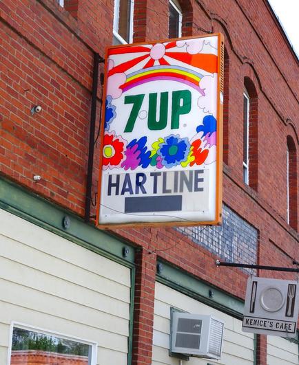 Vintage 7-Up sign with bright colored rainbow and flowers that says the name of the town "Hartline" on it.