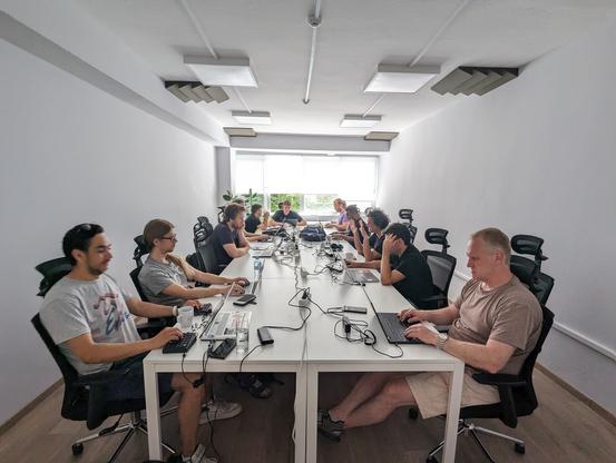 A bunch of people sit around a table, discussing things and working on their laptops