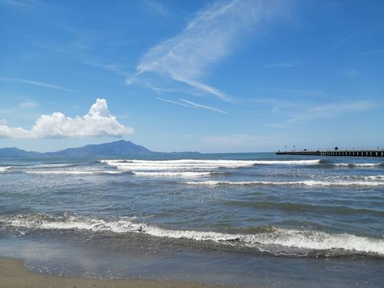 A picture of a beach, with blue but slightly cloudy sky. The island of Ischia is visible in the background