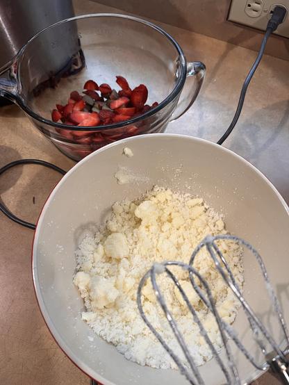 Photo - in the foreground is a ceramic mixing bowl with butter and sugar creamed together, silver beaters poised above it. In the background is a glass mixing bowl full of strawberries and rhubarb.