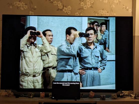 A photo of my TV playing Rodan on laserdisc. An Android tablet is propped up in front of the TV and is displaying English subtitles for the film. 

On screen a group of Japanese men in military uniforms are looking at something off screen using binoculars. 

The tablet is displaying the subtitle "I see the second one! It's coming from the ocean!"