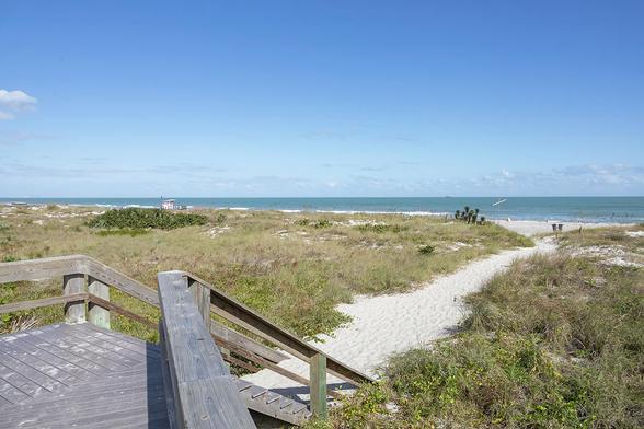 A sunlit pathway beckons at Lori Wilson Park in Cocoa Beach, Florida, guiding wanderers toward the vast expanse of the Atlantic Ocean.