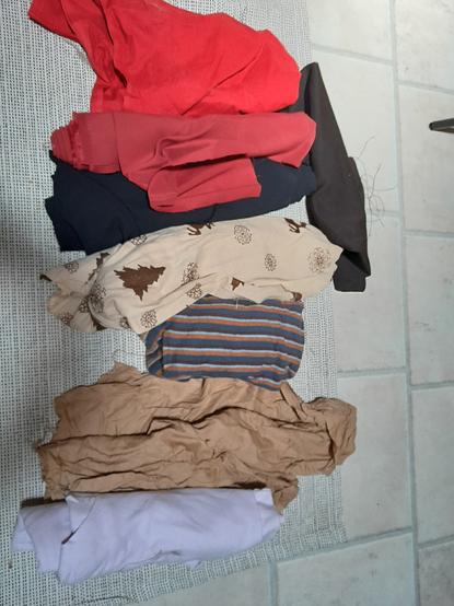 De haut en bas : toile rouge en coton, un rouleau de 2m auquel il manque quelques bouts. Toile rouge en coton, moins vif, rouleau de 2m presque intact. Polyester noir, très extensible, rouleau de 2m intact. Coton imprimé de noel, beige avec des motifs de rennes, flocons et sapins bruns foncés, sûrement un peu moins de 2m. Un jersey rayé bleu marine / brun / bleu clair / orange, un peu plus d'1m. Une chute de soie de coton camel. Un rouleau intact de jersey mauve.