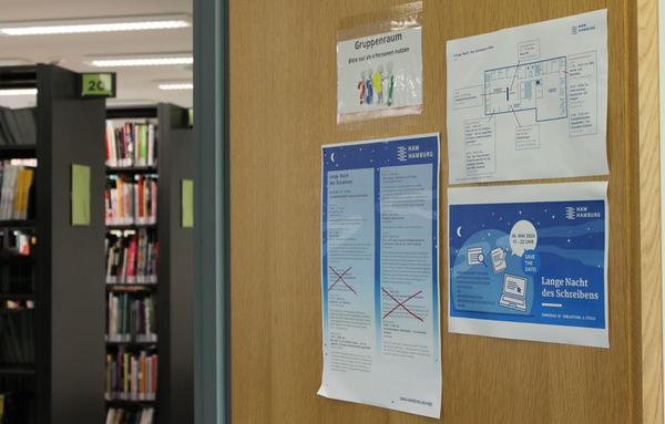 Blick von der Tür eines Seminarraums in die Bibliothek. Man sieht das Programm der Langen Nacht und Bücherregale.