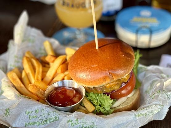 A hamburger with a side of French fries and a small container of ketchup, served on wax paper. A beverage glass is visible in the background.