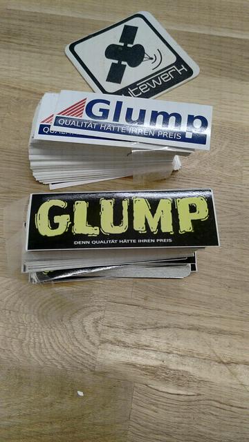 Two large stacks of stickers on a wooden table. Next to them is a coaster withe the bytewerk logo.
The stickers read "GLUMP - Denn Qualität hätte ihren Preis". One of the two designs resembles the logo of Pollin Electronic.