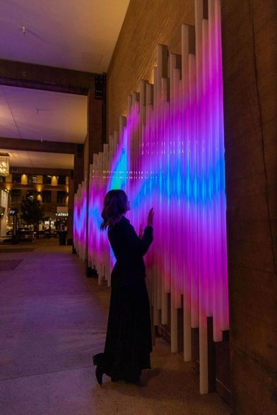 A woman interacting with a light installation on a wall at a pedestrian underpass.