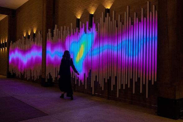 A woman interacting with a light installation on a wall at a pedestrian underpass.