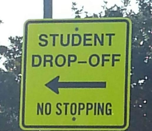 A street sign with an arrow pointing to the left. The sign reads, “Student Drop-off” and “No Stopping.”