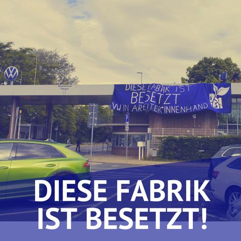 Eine Einfahrt mit großer Überdachung. Darauf ein großes VW-Logo. Am Dach hängt ein riesiges Banner in Lila auf dem steht "Diese Fabrik ist besetzt. VW in Arbeiterinnenhand"
