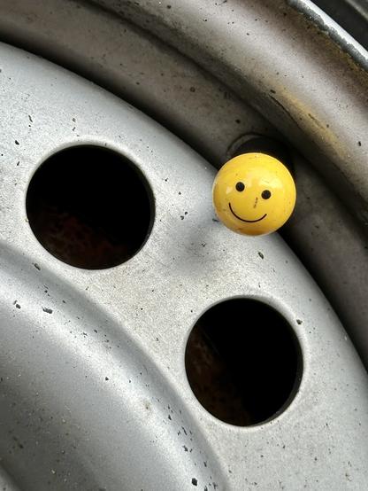 Photo of a tire valve cap shaped like a happy face emoji.

Foto einer Reifenventilkappe, die wie ein glückliches Gesicht-Emoji geformt ist.