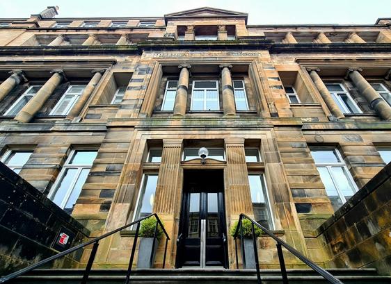 Looking up at the classical style entrance of a large three storey blonde sandstone building.