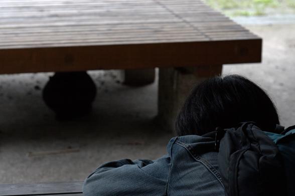 A cat sits underneath a wooden bench, while the photographer drops down and takes a photo of it, ignoring the posing models nearby.