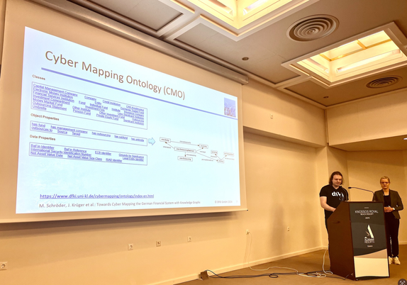 Jacqueline Krüger (right) and Markus Schröder (right) presenting at the ESWC 2024. The cyber mapping ontology is projected on the screen.