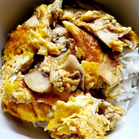 Bowl of steamed rice with mushrooms egg foo yung, in cut up pieces, atop.
