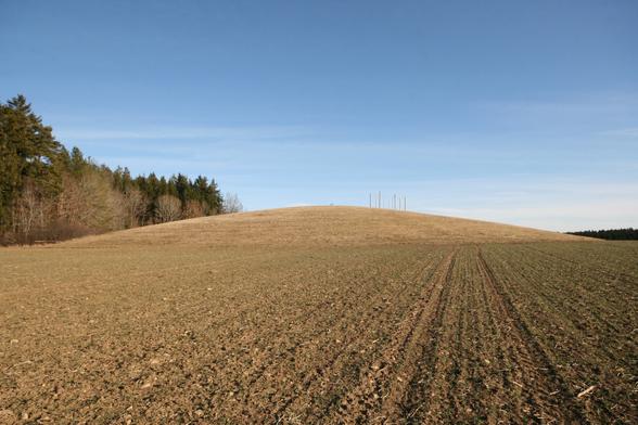 Ein großer, flacher, offensichtlich künstlich aufgeschütteter Hügel ist über einen Ackern hinweg zu sehen