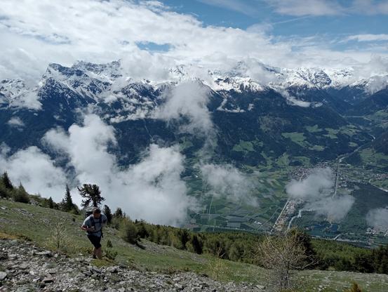 A biologist hiking up a mountain slope with snowcapped mountains in the background.