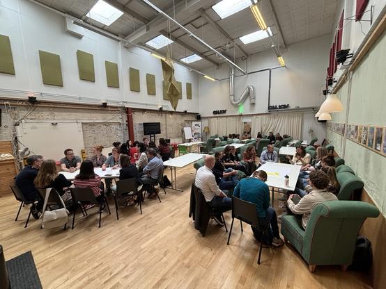 A photo of a room filled with over 40 people in breakout groups discussing answers to the question, 'What's behind the data management plan of the future'