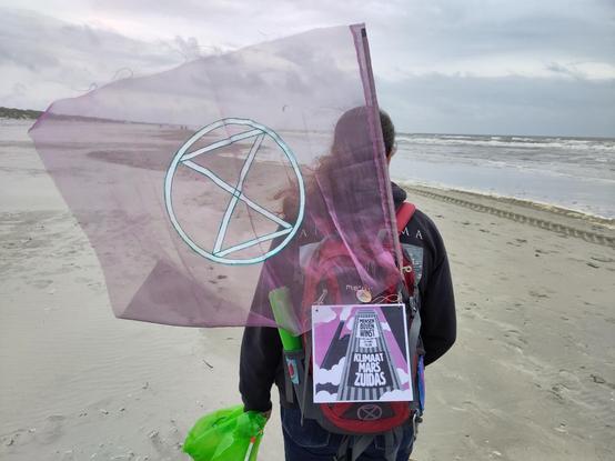 Activist met vlag, bordje, grijper en afvalzak op het strand