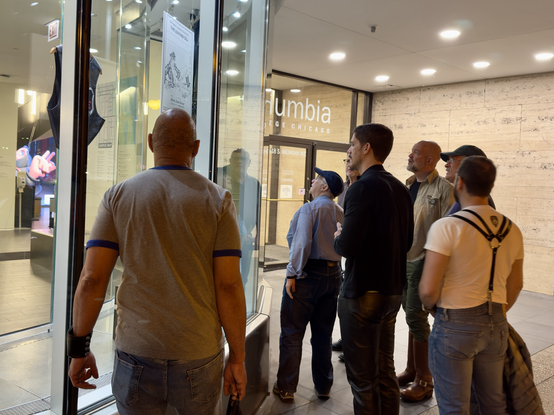 A group of leather community leaders gather around the window display of Leather Legacies