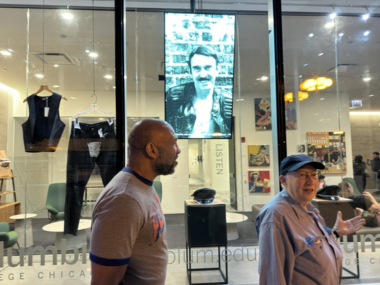 Gayle Rubin and Graylin Thornton discusses leather history in front of a digital display showcasing Chuck Renslow