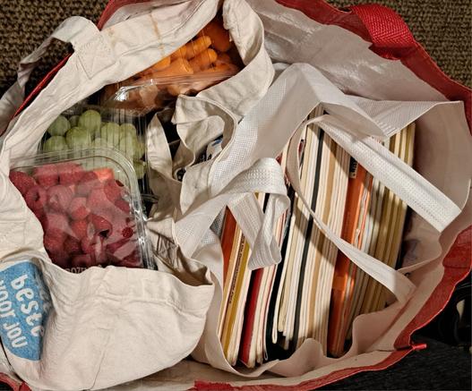 Een boodschappentas met groente en fruit en een tas met een stapel stripboeken.