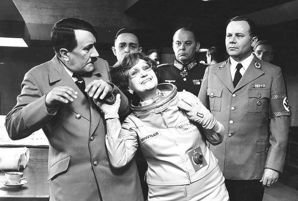 Time-traveling tourist Shirley White (Marie Rosůlková) dragging a bewildered Hitler (František Vicena) in front of her husband's photo camera. DP: Jan Kališ.