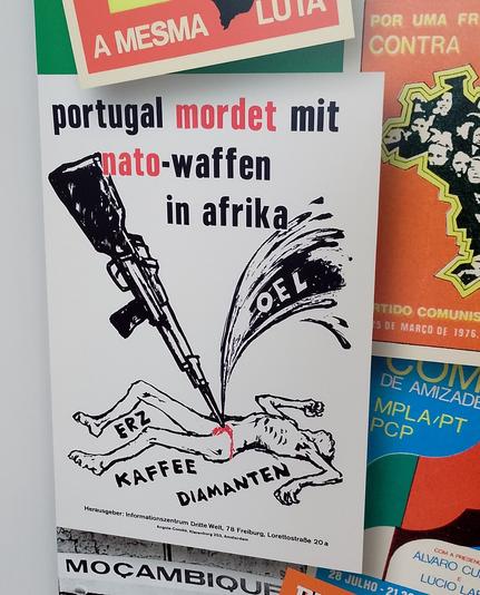 Das Plakat zeigt eine niedergestreckte Person, die von einem Gewehr mit Bajonett durchbohrt wird. Darüber der Titel: portugal mordet mit nato-waffen in afrika. Um die niedergestreckte Person gruppieren sich die Worte Erz, Kaffee und Diamanten.