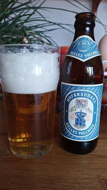 auf einem Tisch steht ein Glas mit hellgelben Bier gefüllt und daneben eine kleine Bierflasche