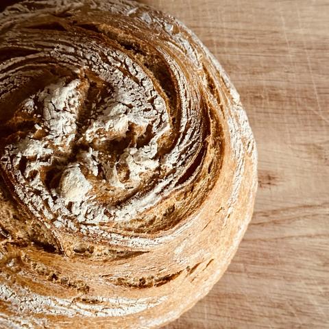 Nahaufnahme eines runden, knusprigen Brotlaibs auf einer Holzunterlage