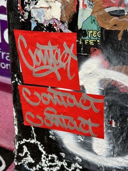 A couple of red pieces of tape stuck to a wall. A tagger wrote "Contact One" in silver paint on the tape before slapping it on the wall.