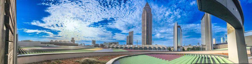 Das Bild zeigt einen Blick von der Dachterrasse des SkylinePlaza Einkaufszentrums in Frankfurt mit zentralem Blick auf den Messeturm und einen blauen Himmel mit weißen Wolken.