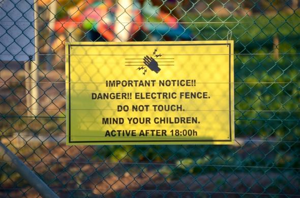 Das Bild zeigt ein Warnschild zum elektrischen Zaun in einer Siedlung in Südafrika