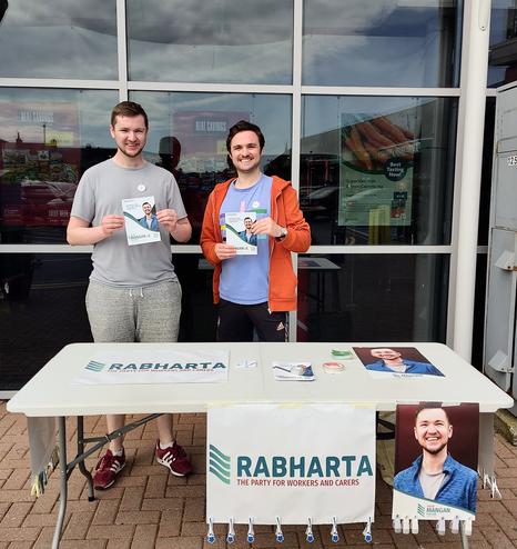 A photo of Killian and his brother Ciarán holding Killian's campaign leaflets while standing behind a table with posters for Killian's local election campaign.