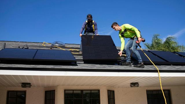 Workers installing solar panels on a roof of a small house