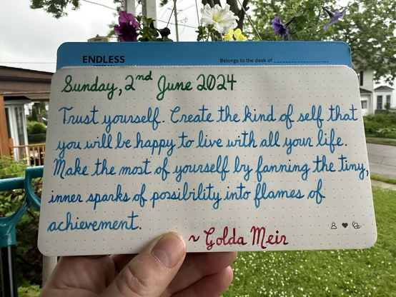 A pen quote of Gilda Meir that reads, “Trust yourself. Create the kind of self that you will be happy to live with all your life. Make the most of yourself by fanning the tiny, inner sparks of possibility into flames of achievement.”  Written in Pelikan Edelstein Adventurine & Topaz, along with Wearingeul Captain Hook.  Hanging plant was made for me by my sister with a non-binary theme. 💛🤍💜🖤