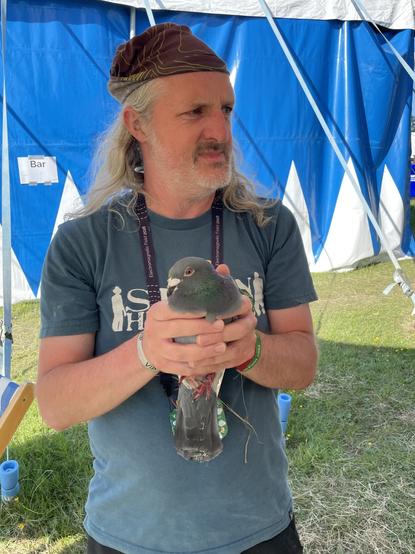Me, holding a racing pigeon in two hands, in the doorway of a big event tent.