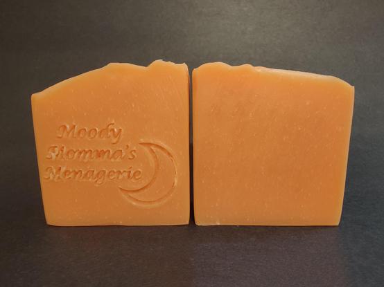 Two light orange colored soaps sitting side by side. The bar on the left is stamped with my branding "Moody Momma's Menagerie" and a crescent moon.
