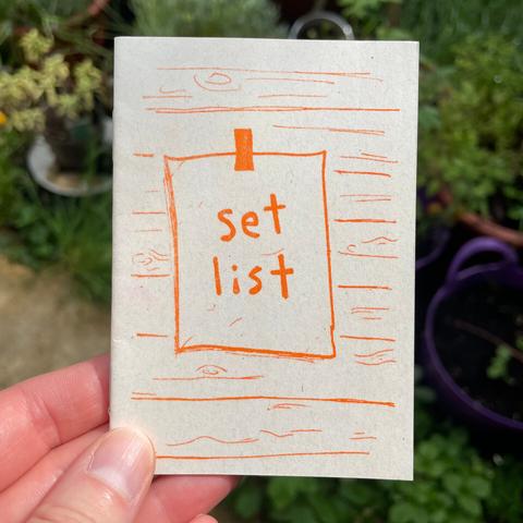 An A7 riso-printed zine with orange ink on grainy-looking cream recycled paper. On the cover it says 'SETLIST'.