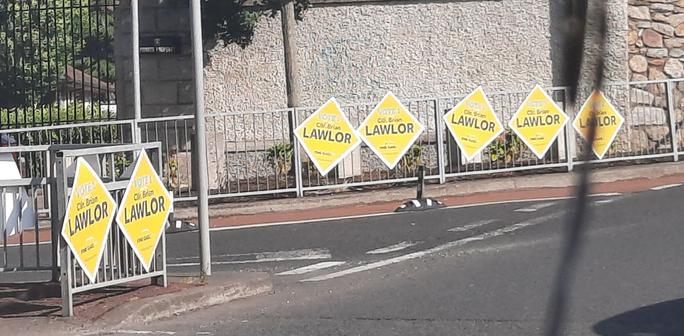Railing at a crossroads with 7 posters right next to each other for Councilor Brian Lawlor for Fine Gael.